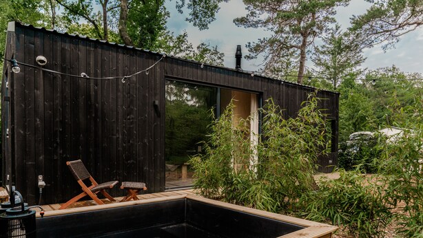 Una cabaña de madera con un jacuzzi, dos sillones de descanso y una pequeña terraza.