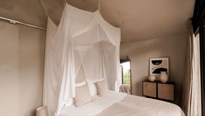 Un dormitorio con cama de dosel, una mesita de noche con lámpara y una mesita de ratán con jarrones decorativos.