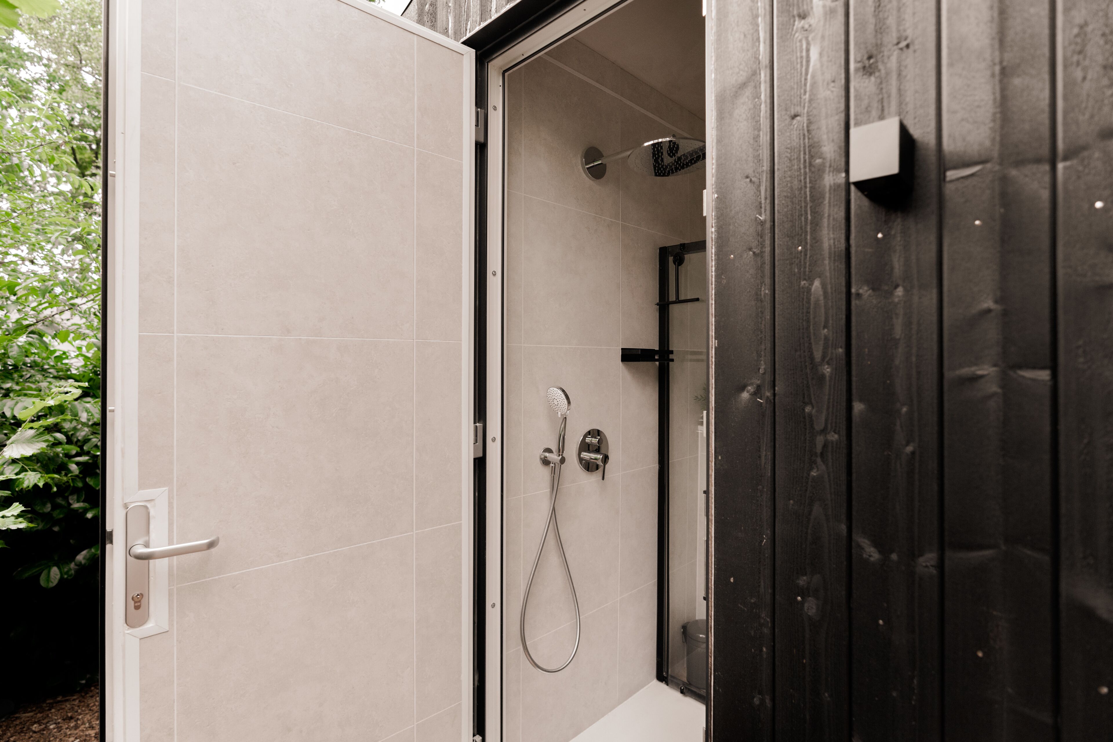 A modern bathroom with a glass shower enclosure, a white bathtub, and a wooden door.