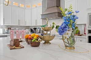 A kitchen with white cabinets, a marble countertop, and a fruit bowl with oranges and apples.