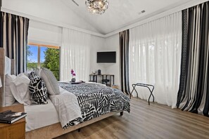 A bedroom with a bed, a TV, a desk, and a chair.