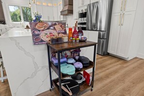 Eine Küche mit Marmorarbeitsplatte, einem Edelstahl-Kühlschrank und einem Holzwagen mit Küchenutensilien.