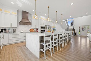 Una cocina moderna con armarios blancos, una isla central con asientos y una escalera que conduce a un nivel superior.