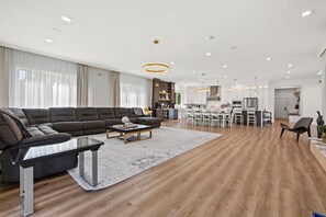 Una sala de estar moderna con un sofá modular, una mesa de centro y un comedor con sillas blancas, con una cocina al fondo.