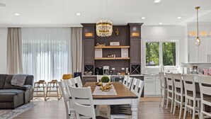 Una cocina moderna con armarios blancos, un comedor con mesa de madera y sillas blancas, y un candelabro sobre la mesa.
