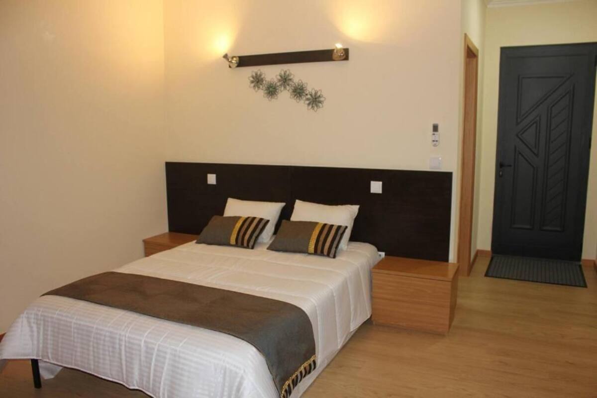 A neatly arranged bedroom with a large bed, bedside tables, a wall-mounted light fixture, and a door.