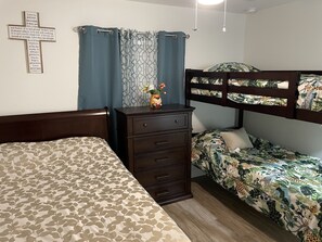 Ein Schlafzimmer mit einem Etagenbett, einem Einzelbett, einem Schminktisch und einem Kreuz an der Wand.