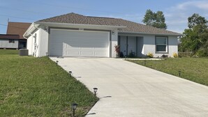 A single-story house with a white garage door, a sloped roof, and a front yard with a sidewalk and street lamps.