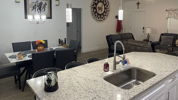 A modern kitchen with granite countertops, a stainless steel sink, and a dining area with a table and chairs.