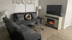 A modern living room with a sectional sofa, a fireplace, a flat-screen TV, and a glass coffee table.