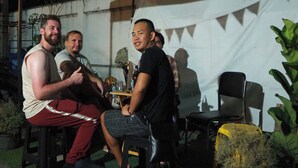 A group of people seated at an outdoor table under a tent with triangular bunting. - Bed Space Hostel  (Bangkok)