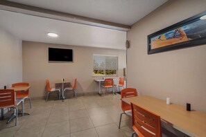 A dining area with tables and chairs, a window with blinds, a mounted television, and a framed picture on the wall. - Surestay by Best Western Williams - Grand Canyon (Williams)