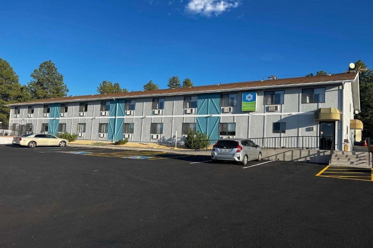 A motel with a row of rooms, a parking lot, and a clear blue sky.