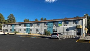 Un motel con una hilera de habitaciones, un estacionamiento y un cielo azul despejado.