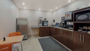 Cocina compacta con refrigerador, microondas, cafetera y un lavamanos pequeño.