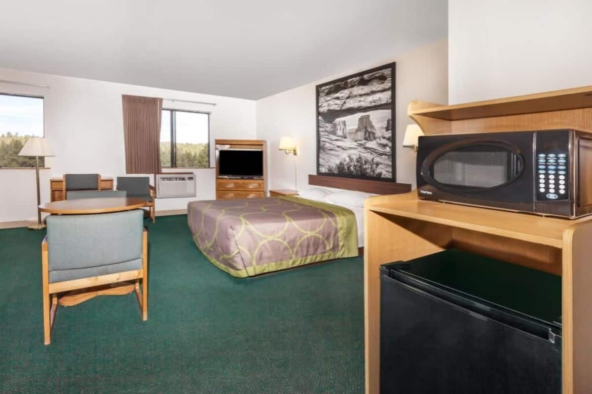 A hotel room with a bed, a desk with a computer, a microwave, and a refrigerator.