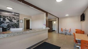 A hotel reception area with a counter, a large framed picture, a television, and a dining area with orange chairs. - Surestay by Best Western Williams - Grand Canyon (Williams)