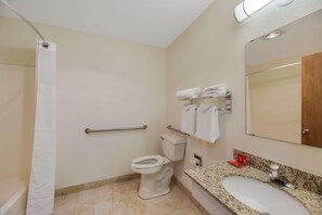 Un baño con inodoro, cortina de ducha, barras de apoyo, lavamanos con espejo y toallero.