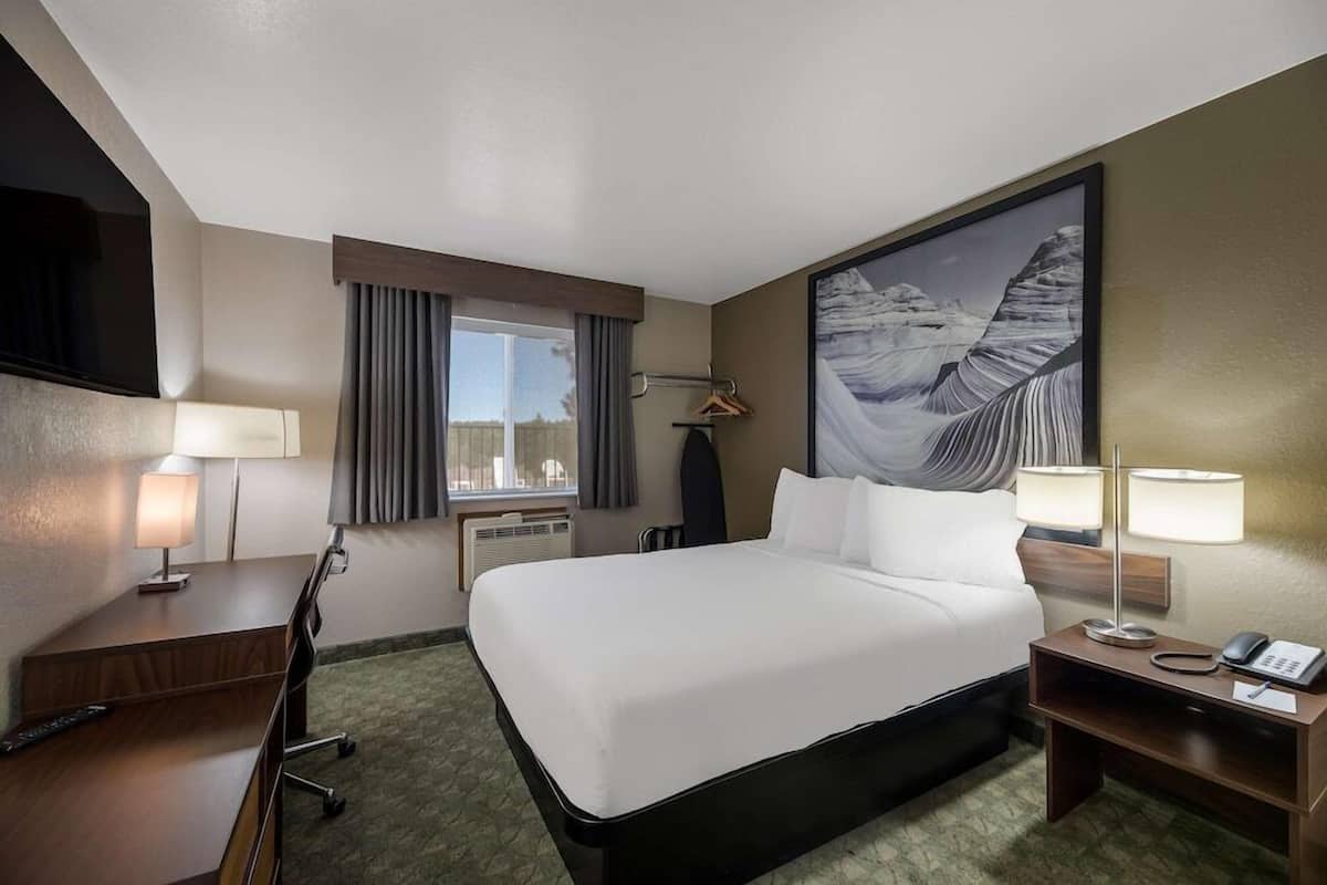 A hotel room with a bed, desk, chair, lamps, and a large painting on the wall.