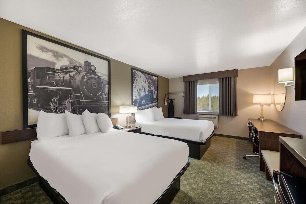 A hotel room with two beds, a desk, a chair, a lamp, and a large framed picture of a train.