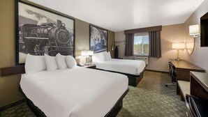 Habitación de hotel con dos camas, un escritorio, una silla, una lámpara y un cuadro grande con una imagen de un tren.