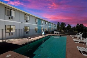 A hotel with a swimming pool, lounge chairs, and a fence.