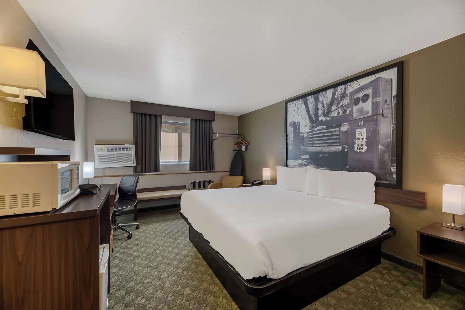 Een hotelkamer met een groot bed, een bureau met een computer, een stoel, een televisie en een groot raam.
