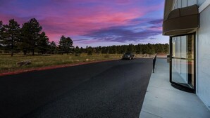 A modern building with a glass facade, a paved driveway, and a vehicle parked in the distance. - Surestay by Best Western Williams - Grand Canyon (Williams)