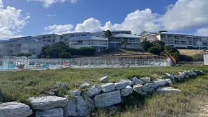 A beachfront hotel with multiple balconies, a swimming pool, and a rocky foreground. - French Ocean View , Beach and Pool (Cul-de-Sac)