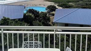A balcony with a view of a beach, a swimming pool, and a distant mountain range. - French Ocean View , Beach and Pool (Cul-de-Sac)