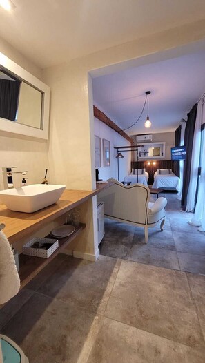 A hotel room with a large bed, a bedside table, a mirror, a TV, and a bathroom with a sink and shower. - La Belle San Isidro Lofts (Acassuso)