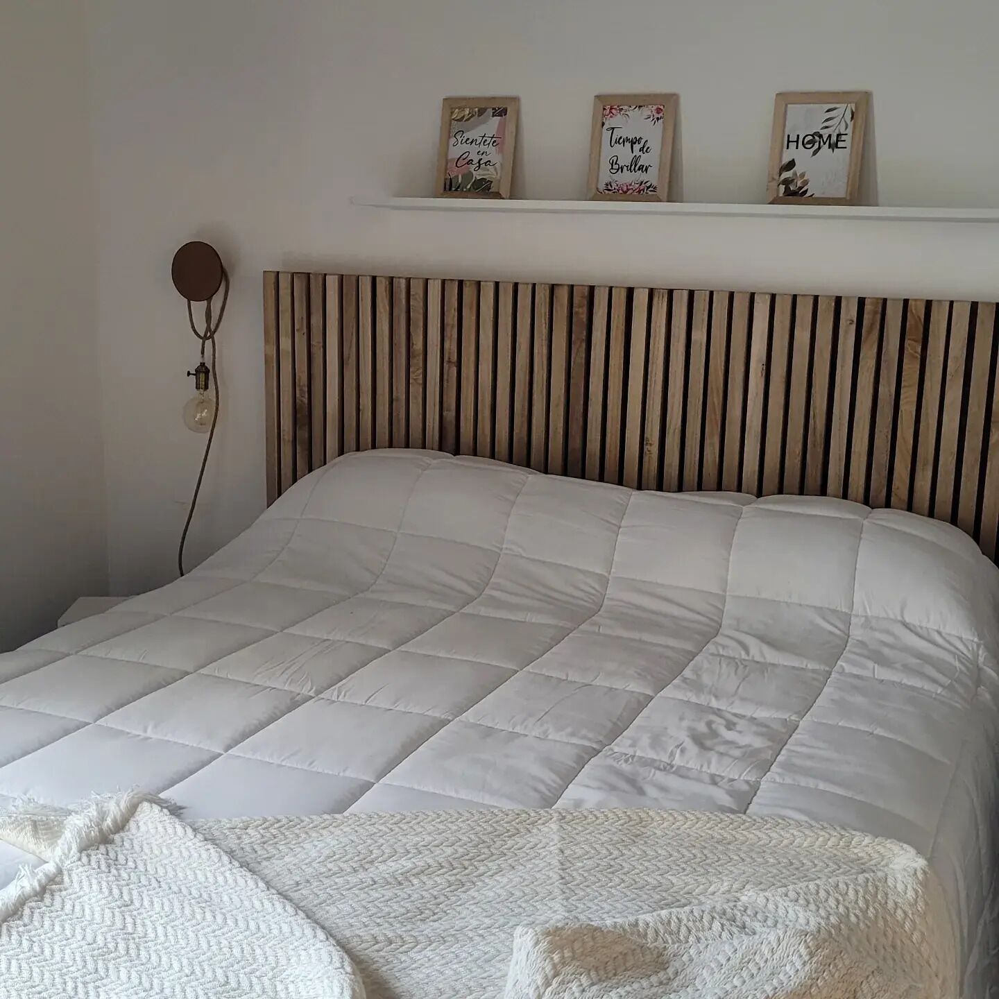 A bed with a wooden slat headboard, a white quilted bedspread, and a white throw blanket at the foot of the bed.