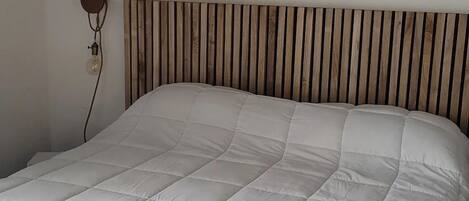 A bed with a wooden slat headboard, a white quilted bedspread, and a white throw blanket at the foot of the bed.