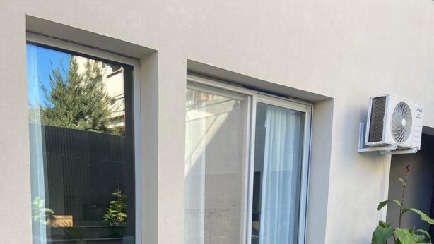 Un espacio exterior con dos sillas, una mesa, un ventanal corredero y una planta en maceta.