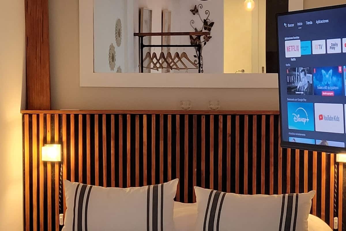Quarto de hotel com cama grande, cabeceira de madeira e TV fixada exibindo serviços de streaming.