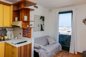 Een compacte kamer met een kitchenette, een bank, een schilderij en uitzicht op een jachthaven.