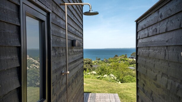 A wooden exterior with a glass door leading to a balcony overlooking a sea view. - Nice home in Asnæs with sauna (Asnæs)