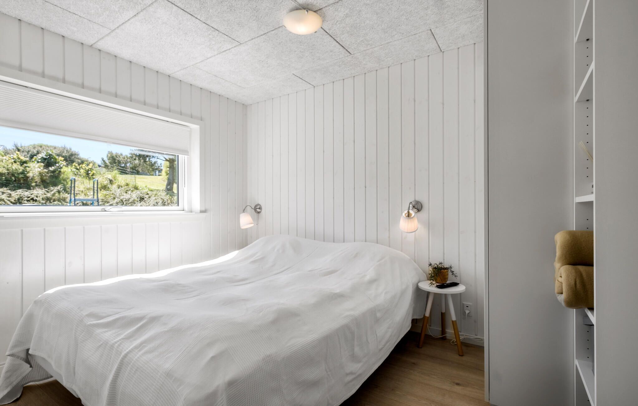 Une chambre avec un grand lit, une fenêtre et une petite table de chevet avec une lampe.