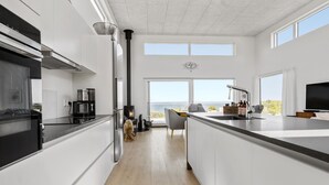 A modern kitchen with a central island, a stove, and a large window overlooking a scenic view. - Nice home in Asnæs with sauna (Asnæs)