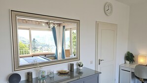Una camera da letto con uno specchio grande, una cassettiera, una scrivania con una sedia, una sveglia e vista sul verde.