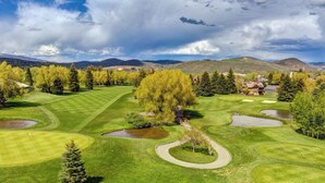 Un campo de golf con varios hoyos, un club de campo y árboles circundantes.