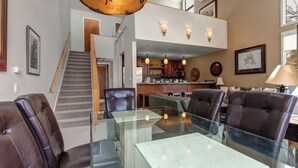 Un salón amplio con una mesa de centro de vidrio, sillones de cuero y una escalera que conduce a un nivel superior.