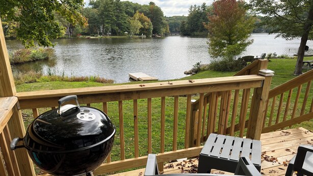 A deck with a grill, chairs, and a view of a lake.