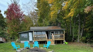A cabin with a deck, two blue Adirondack chairs, a red kayak, and a wooden dock.