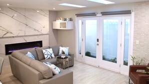 Un salon moderne avec un canapé beige, une cheminée, une petite table d’appoint et une porte-fenêtre coulissante donnant sur un balcon.