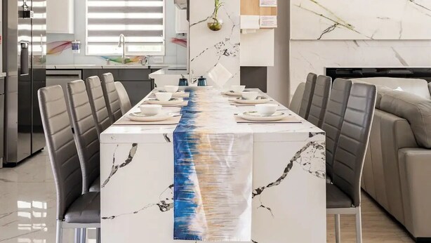 Une cuisine moderne avec un îlot en marbre, des chaises grises et une table à manger dressée pour six personnes.