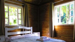 A wooden cabin room with a bed, a nightstand, and windows with curtains. - Beautiful chalet overlooking Pico do Marumbi (Morretes)