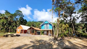 A two-story building with a blue and orange exterior, surrounded by tropical vegetation and palm trees. - Beautiful chalet overlooking Pico do Marumbi (Morretes)