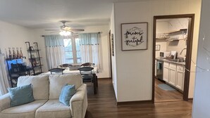A living room with a sofa, a dining table, and a kitchen area visible through an open doorway. - Trailside Terrace 
Private access to tunnel vision trial (Bella Vista)