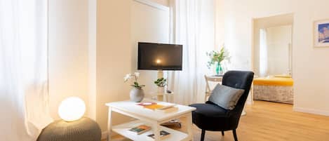 A modern living room with a flat-screen TV, a round ottoman, a white coffee table, a black armchair, and a yellow sofa.